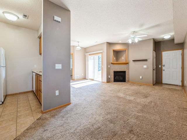 1106 N 6th St Unit 42, Indianola, IA 50125 - unfurnished living room featuring ceiling fan, a textured ceiling, a tiled fireplace, light carpet, and light tile patterned floors