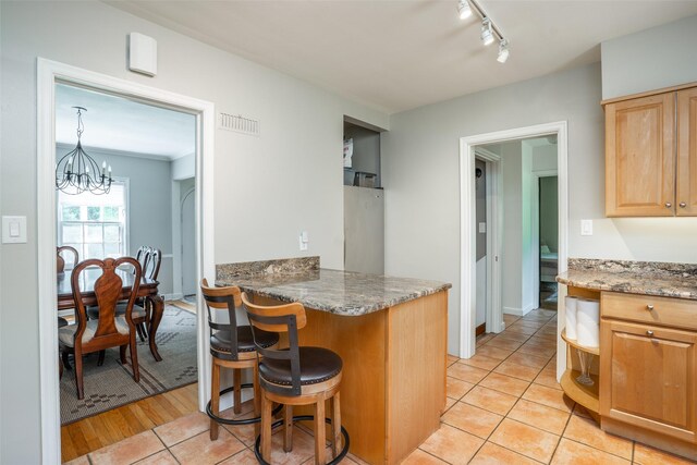 5625 Kingman Ave, Des Moines, IA 50311 - kitchen with a breakfast bar area, a peninsula, a chandelier, light brown cabinetry, and light tile patterned flooring