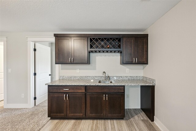 629 Mallard Pointe Dr NW, Bondurant, IA 50035 - kitchen with dark brown cabinetry, light stone countertops, light wood-style floors, and a textured ceiling