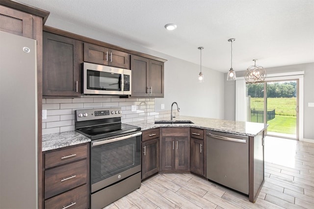 2017 NE Heritage Dr, Grimes, IA 50111 - kitchen with stainless steel appliances, a peninsula, dark brown cabinets, tasteful backsplash, and light stone countertops