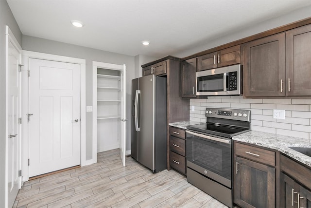 2017 NE Heritage Dr, Grimes, IA 50111 - kitchen with stainless steel appliances, dark brown cabinetry, tasteful backsplash, light stone countertops, and light wood-type flooring