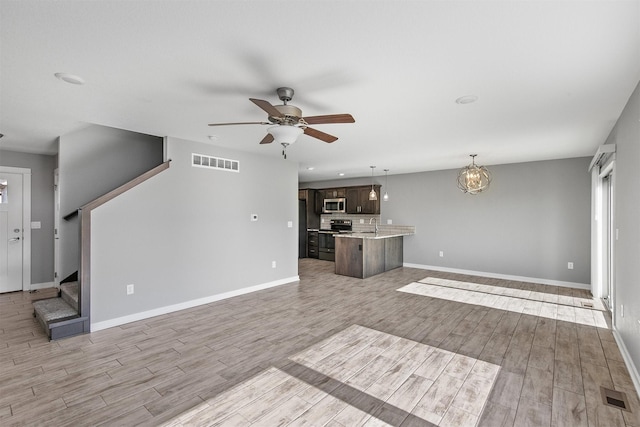 2017 NE Heritage Dr, Grimes, IA 50111 - unfurnished living room with light wood-type flooring, ceiling fan, a chandelier, and stairs