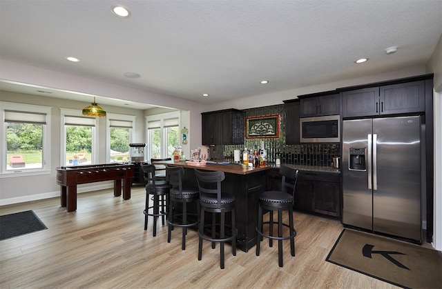 11174 NW 108th Ct, Granger, IA 50109 - kitchen with appliances with stainless steel finishes, a breakfast bar area, light wood finished floors, decorative backsplash, and wood counters