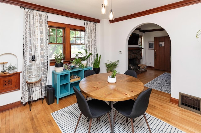 2220 York St, Des Moines, IA 50316 - dining area featuring arched walkways, a brick fireplace, light wood-style floors, and crown molding