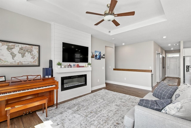 2845 SE Bluestem Dr, Waukee, IA 50263 - living room featuring a ceiling fan, wood finished floors, a raised ceiling, recessed lighting, and a glass covered fireplace