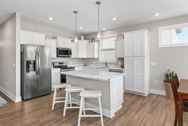 2845 SE Bluestem Dr, Waukee, IA 50263 - kitchen featuring stainless steel appliances, a kitchen island, dark wood finished floors, white cabinetry, and a kitchen bar
