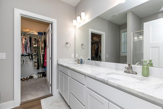 2845 SE Bluestem Dr, Waukee, IA 50263 - full bathroom featuring double vanity, a walk in closet, wood finished floors, and a stall shower