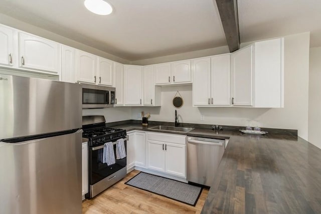 3901 Lawnwoods Dr, Des Moines, IA 50310 - kitchen featuring appliances with stainless steel finishes, dark countertops, light wood finished floors, beam ceiling, and white cabinets