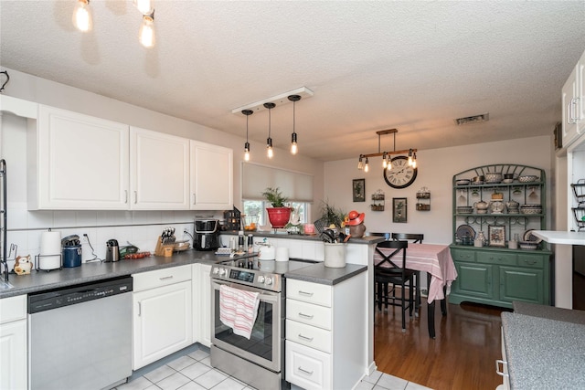 729 SE 3rd St, Ankeny, IA 50021 - kitchen with appliances with stainless steel finishes, a peninsula, dark countertops, white cabinets, and a textured ceiling
