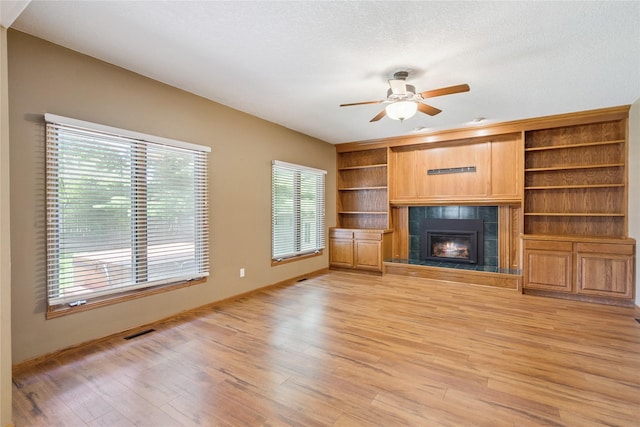 303 Trevor Ct, Norwalk, IA 50211 - unfurnished living room featuring a tile fireplace, light wood-style flooring, ceiling fan, and built in shelves