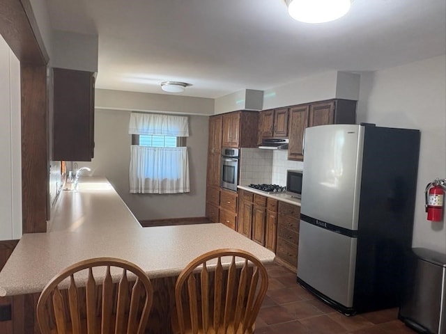 3909 75th St, Urbandale, IA 50322 - kitchen with appliances with stainless steel finishes, light countertops, under cabinet range hood, decorative backsplash, and a peninsula