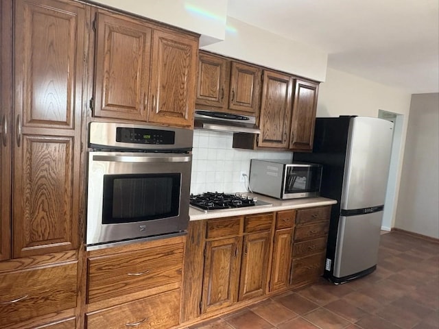 3909 75th St, Urbandale, IA 50322 - kitchen with stainless steel appliances, tasteful backsplash, light countertops, under cabinet range hood, and brown cabinetry