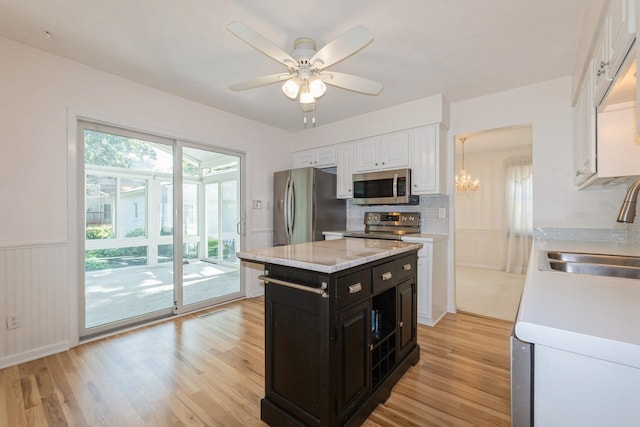 4511 67th St, Urbandale, IA 50322 - kitchen with stainless steel appliances, dark cabinets, white cabinetry, light wood-style floors, and wainscoting