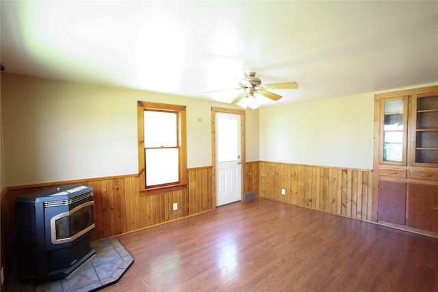 24388 250th St, Eldora, IA 50627 - empty room featuring a wainscoted wall, a wood stove, wood finished floors, a ceiling fan, and wood walls
