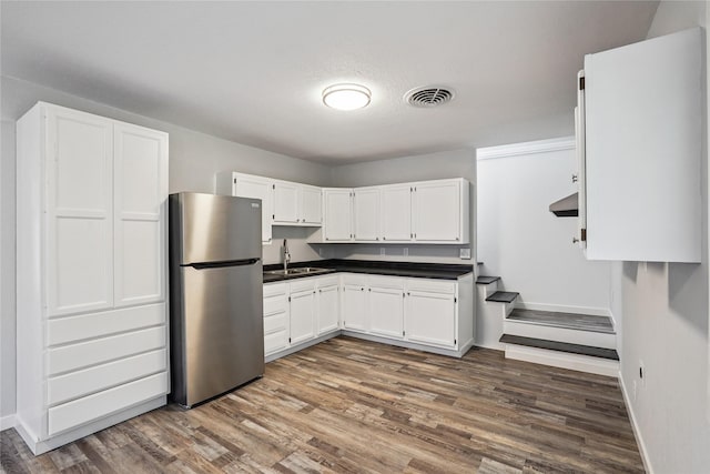 9 1st St, Collins, IA 50055 - kitchen with freestanding refrigerator, wood finished floors, white cabinetry, and dark countertops