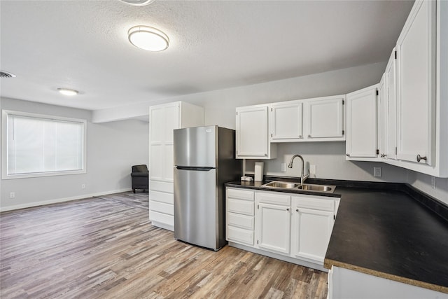 9 1st St, Collins, IA 50055 - kitchen with freestanding refrigerator, dark countertops, light wood-type flooring, white cabinetry, and a textured ceiling