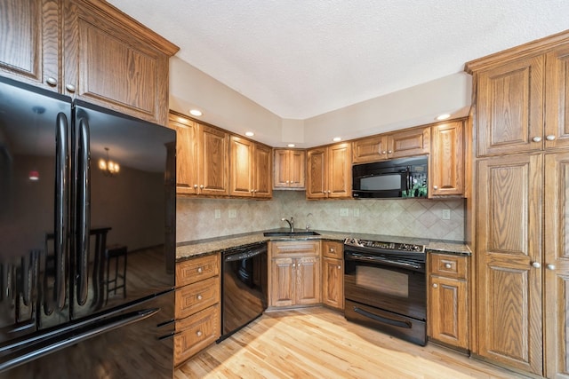 2424 Guenever Ct, Altoona, IA 50009 - kitchen featuring black appliances, brown cabinetry, light wood-type flooring, dark stone counters, and a textured ceiling