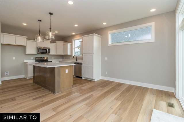 1435 Locust St, Waukee, IA 50263 - kitchen with stainless steel appliances, a center island, light wood-style floors, white cabinets, and light countertops