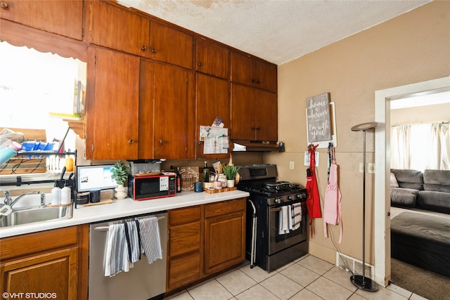 705 E Miller Ave, Des Moines, IA 50315 - kitchen with stainless steel appliances, under cabinet range hood, light countertops, light tile patterned floors, and brown cabinetry