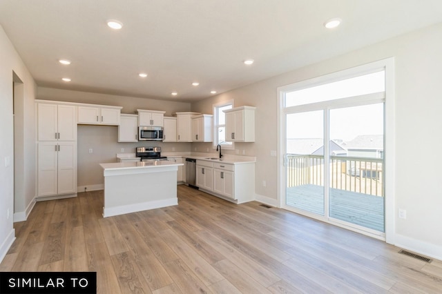 1425 Locust St, Waukee, IA 50263 - kitchen with stainless steel appliances, light wood-style floors, a kitchen island, white cabinets, and recessed lighting