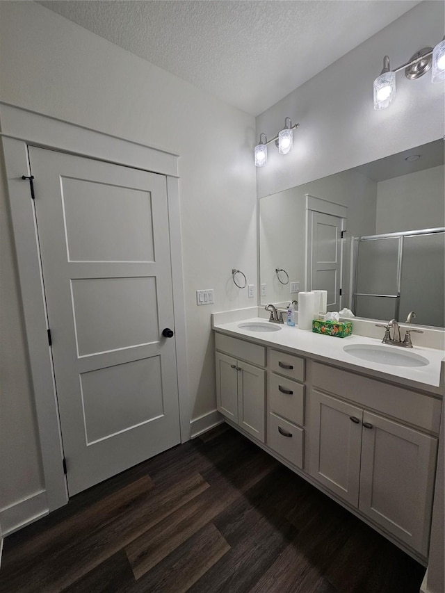 1108 28th St, Perry, IA 50220 - full bathroom featuring wood finished floors, double vanity, a shower stall, and a textured ceiling