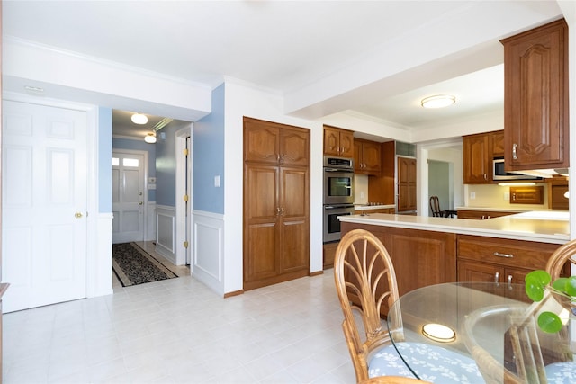 1809 79th St, Windsor Heights, IA 50324 - kitchen featuring appliances with stainless steel finishes, light countertops, ornamental molding, brown cabinets, and a wainscoted wall