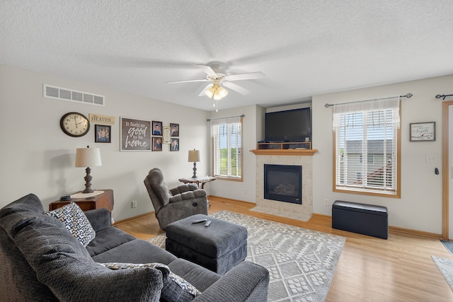 2618 13th St SW, Altoona, IA 50009 - living room featuring a ceiling fan, a tile fireplace, light wood finished floors, and a textured ceiling