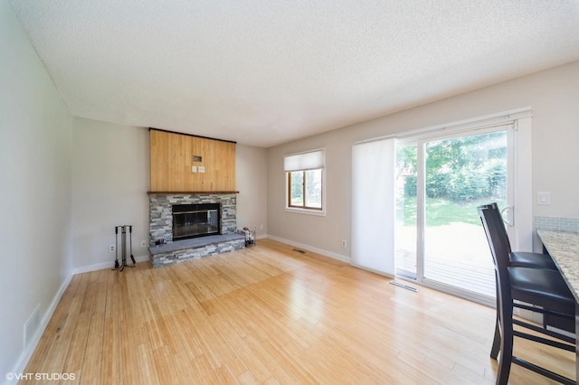 2729 Meadow Point Ct, West Des Moines, IA 50265 - unfurnished living room featuring light wood finished floors, a stone fireplace, and a textured ceiling