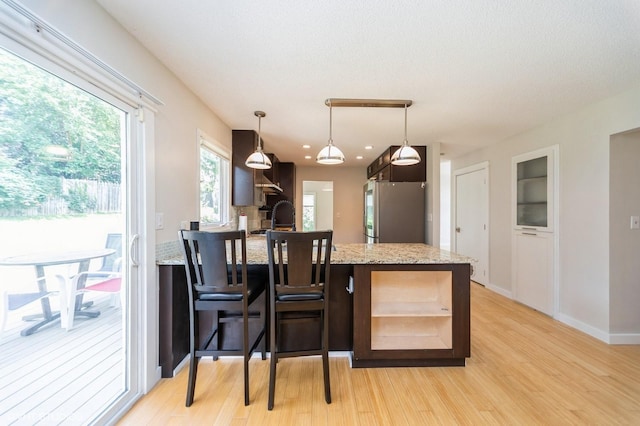 2729 Meadow Point Ct, West Des Moines, IA 50265 - kitchen with freestanding refrigerator, light wood-type flooring, a peninsula, light stone countertops, and dark brown cabinets