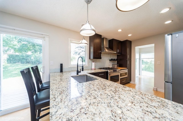 2729 Meadow Point Ct, West Des Moines, IA 50265 - kitchen featuring appliances with stainless steel finishes, wall chimney range hood, light stone countertops, decorative light fixtures, and dark brown cabinetry