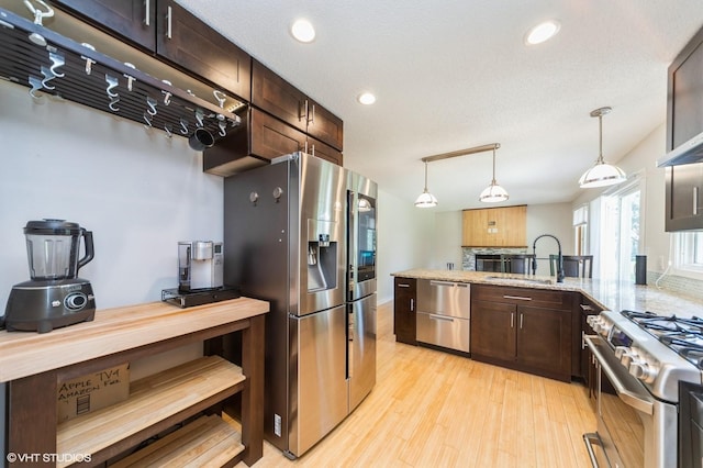 2729 Meadow Point Ct, West Des Moines, IA 50265 - kitchen featuring appliances with stainless steel finishes, dark brown cabinets, light wood-style floors, decorative light fixtures, and a peninsula