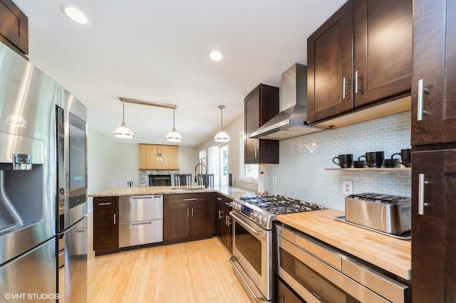 2729 Meadow Point Ct, West Des Moines, IA 50265 - kitchen featuring stainless steel appliances, wall chimney range hood, light wood-style floors, dark brown cabinets, and decorative backsplash