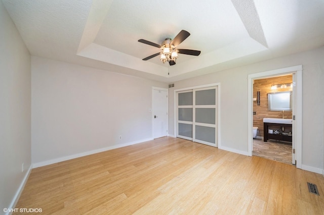 2729 Meadow Point Ct, West Des Moines, IA 50265 - unfurnished bedroom featuring a tray ceiling, light wood-type flooring, ensuite bathroom, and ceiling fan