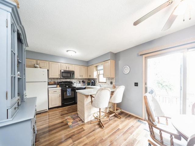 401 NW Valley View Dr, Grimes, IA 50111 - kitchen featuring black range with electric cooktop, freestanding refrigerator, stainless steel microwave, cream cabinetry, and backsplash