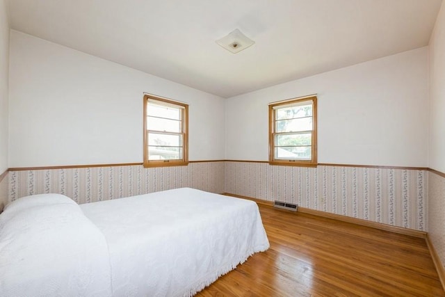 7210 Beechwood Dr, Urbandale, IA 50322 - bedroom featuring a wainscoted wall, wallpapered walls, wood finished floors, and multiple windows