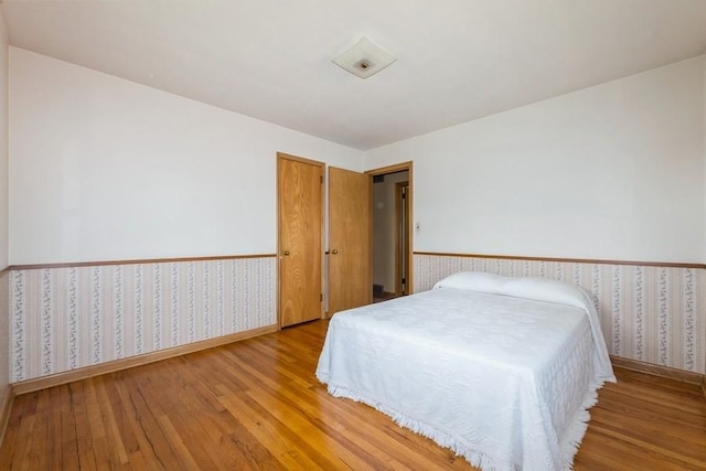 7210 Beechwood Dr, Urbandale, IA 50322 - bedroom featuring wallpapered walls, wood-type flooring, and a wainscoted wall