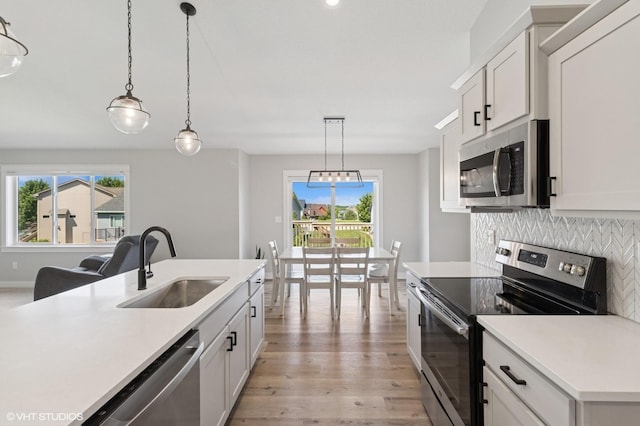 2670 Long Ave, Van Meter, IA 50261 - kitchen featuring appliances with stainless steel finishes, light wood-style flooring, light countertops, hanging light fixtures, and decorative backsplash
