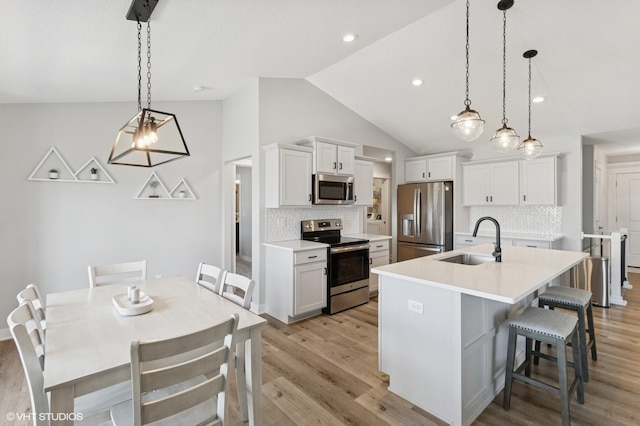 2670 Long Ave, Van Meter, IA 50261 - kitchen featuring stainless steel appliances, vaulted ceiling, decorative backsplash, light wood-style flooring, and an island with sink