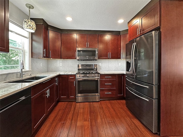 2814 Chicago Ave, Des Moines, IA 50317 - kitchen featuring stainless steel appliances, dark wood-style floors, light stone counters, decorative backsplash, and decorative light fixtures