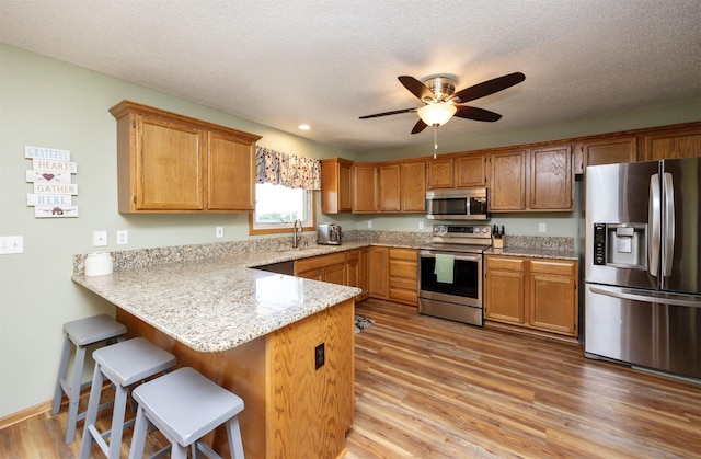 5030 Oakcreek Dr, Norwalk, IA 50211 - kitchen featuring stainless steel appliances, a peninsula, ceiling fan, light wood finished floors, and a kitchen bar