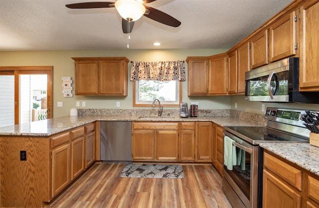 5030 Oakcreek Dr, Norwalk, IA 50211 - kitchen with appliances with stainless steel finishes, a peninsula, light wood finished floors, ceiling fan, and brown cabinetry