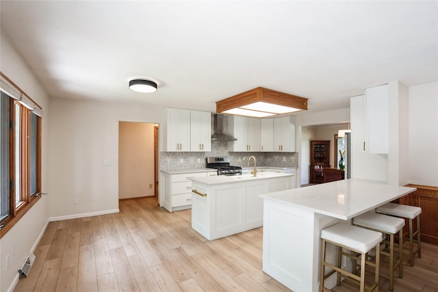1711 Plaza Cir, Windsor Heights, IA 50324 - kitchen with wall chimney range hood, stainless steel appliances, a kitchen island with sink, light wood finished floors, and backsplash
