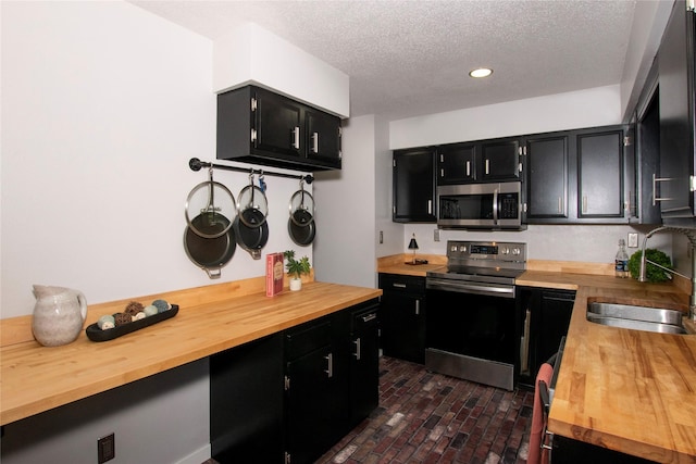 500 Scandia Ave, Des Moines, IA 50315 - kitchen with stainless steel appliances, wood counters, dark cabinets, brick flooring, and a textured ceiling