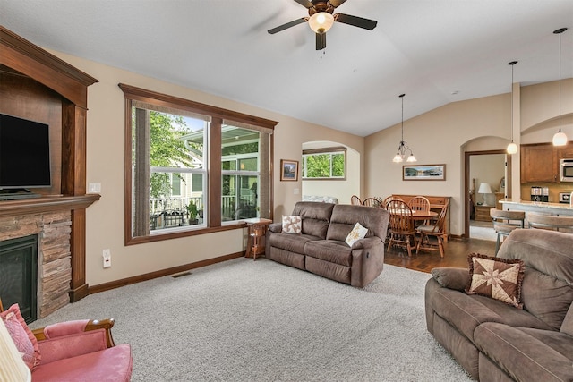 6054 Bradford Ln, Johnston, IA 50131 - carpeted living room featuring arched walkways, a stone fireplace, vaulted ceiling, and plenty of natural light