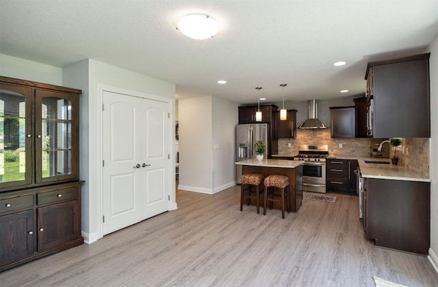 296 S 82nd St, West Des Moines, IA 50266 - kitchen with appliances with stainless steel finishes, wall chimney exhaust hood, dark brown cabinetry, a breakfast bar area, and light wood-style flooring
