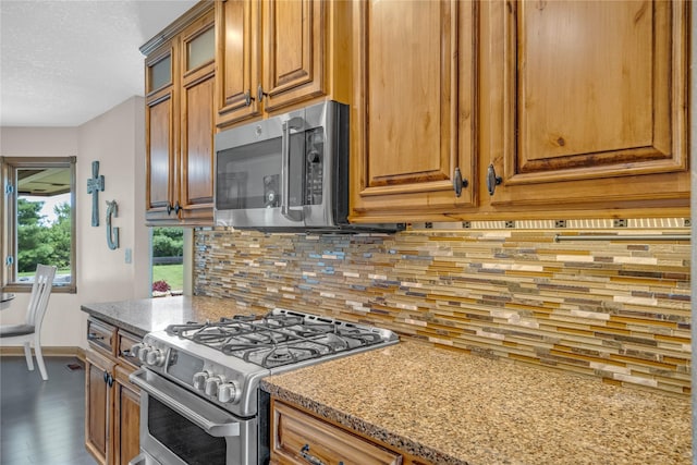 904 Pleasant St SE, Bondurant, IA 50035 - kitchen with appliances with stainless steel finishes, brown cabinets, glass insert cabinets, decorative backsplash, and a textured ceiling