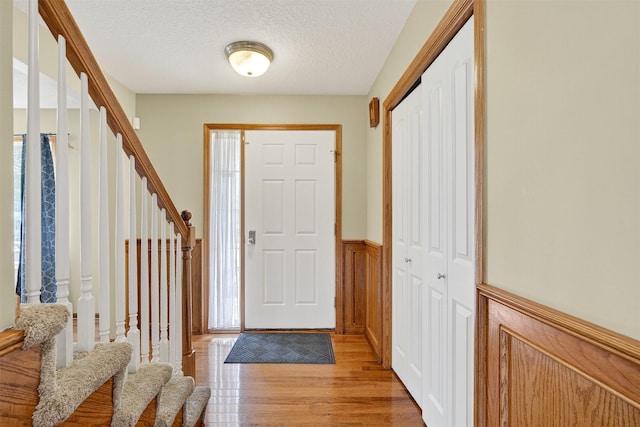 3413 Brook Run Dr, Des Moines, IA 50317 - foyer featuring stairs, light wood-style floors, a wainscoted wall, and a textured ceiling