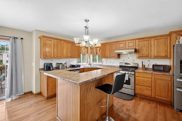 3413 Brook Run Dr, Des Moines, IA 50317 - kitchen featuring appliances with stainless steel finishes, light wood-style flooring, under cabinet range hood, a chandelier, and a center island