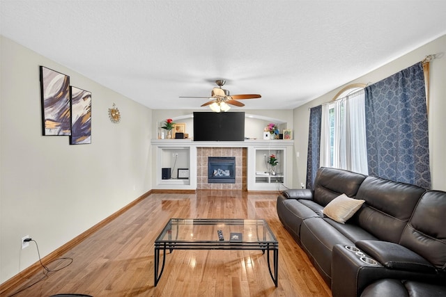 3413 Brook Run Dr, Des Moines, IA 50317 - living room with light wood-style flooring, a ceiling fan, a textured ceiling, and a tiled fireplace