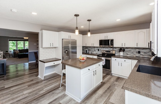 2507 135th St, Urbandale, IA 50323 - kitchen with appliances with stainless steel finishes, light wood finished floors, decorative backsplash, white cabinetry, and a kitchen island